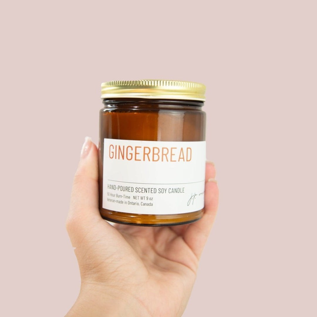 Hand holding a gingerbread scented candle jar against a pink background