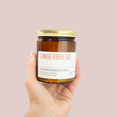 Hand holding a gingerbread scented candle jar against a pink background
