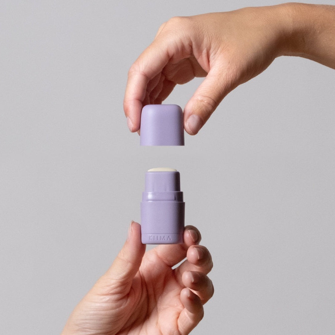 Two hands holding a purple stick of deodorant against a gray background