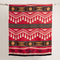 A Kwe Indigenous reversible blanket featuring bold red, black, white, and ochre geometric patterns, hanging from a natural branch. This culturally significant blanket is available in Ottawa, Ontario, Canada.
