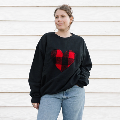 A black sweatshirt with a large, red and black buffalo plaid heart design in the center. 
