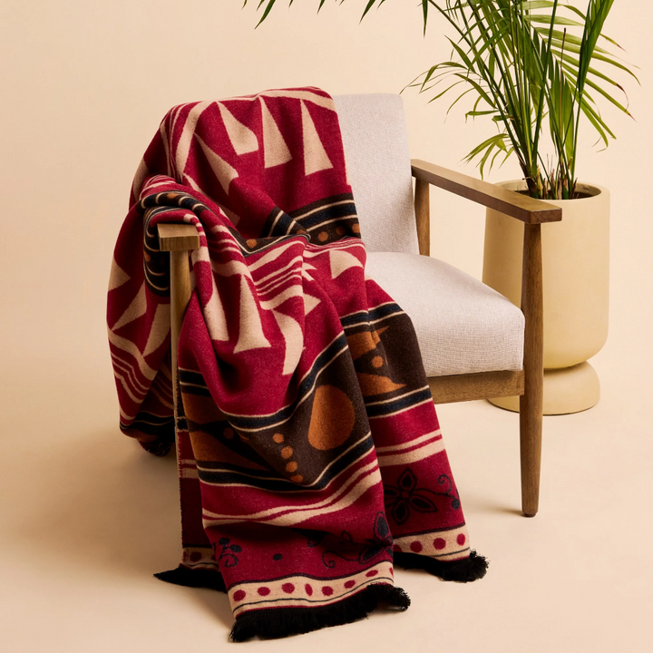 A Kwe Indigenous reversible blanket featuring bold red, black, white, and ochre geometric patterns, hanging from a natural branch. This culturally significant blanket is available in Ottawa, Ontario, Canada.