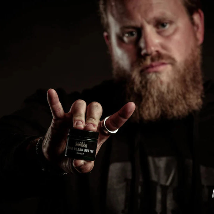 A dark green glass jar with a black lid. The jar is filled with beard butter and has a black label with the text 
