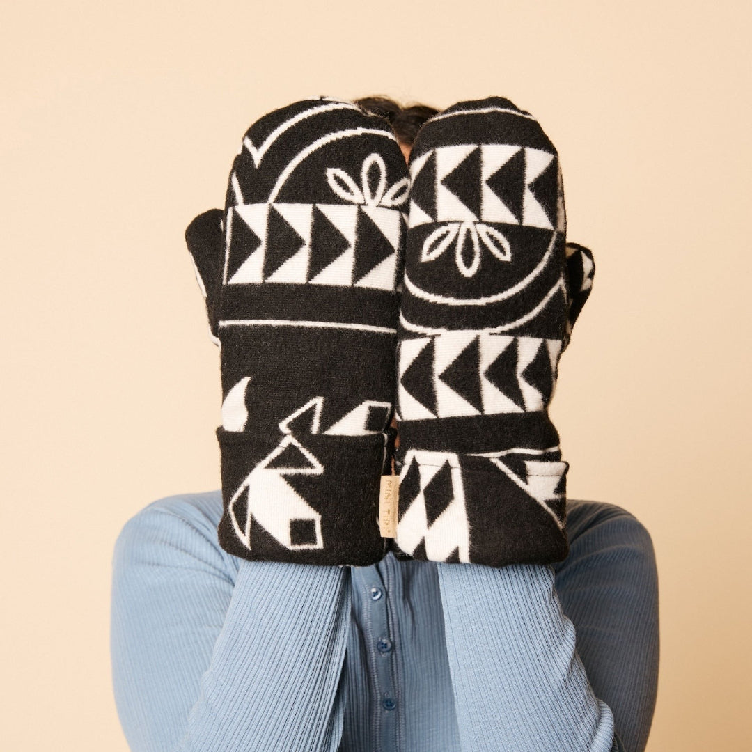 Person wearing black and white patterned mittens on a beige background