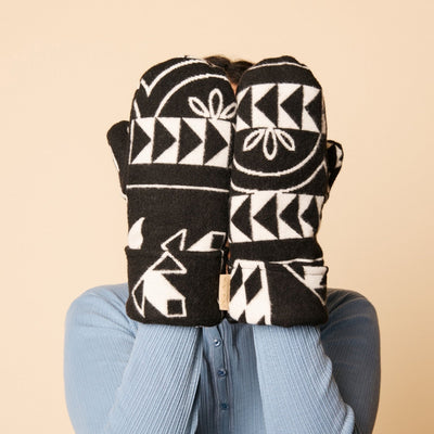 Person wearing black and white patterned mittens on a beige background