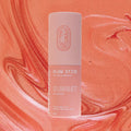 Sunset Glow Stick, a solid highlighter makeup stick in a warm coral pink sunset colour. It is presented in a cardboard tube, with a pull off top.