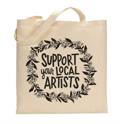 Beige tote bag with 'Support your local artists' text and floral design on a white background