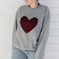 Woman wearing a gray sweater with a red heart design against a white background