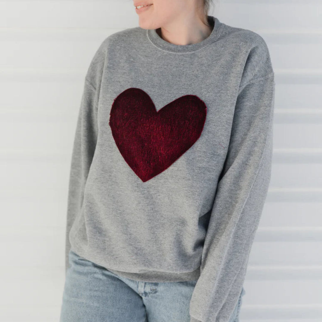 Woman wearing a gray sweater with a red heart design against a white background
