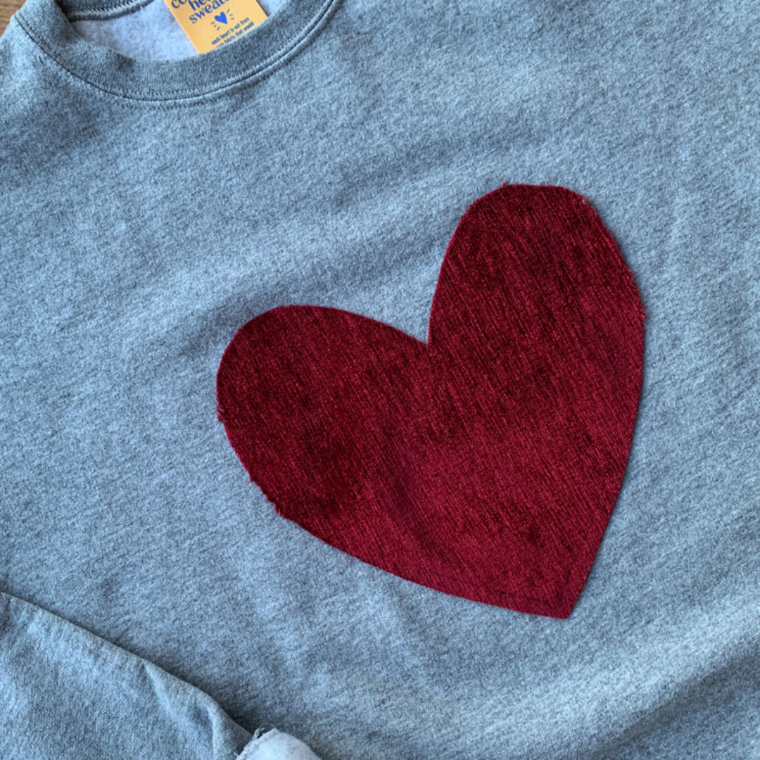 Gray sweatshirt with a red heart design on a wooden surface