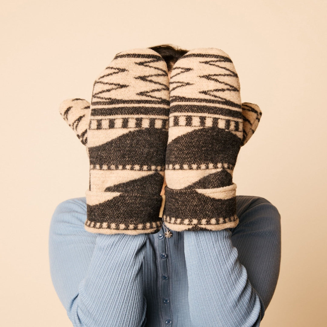Person wearing patterned mittens on a beige background