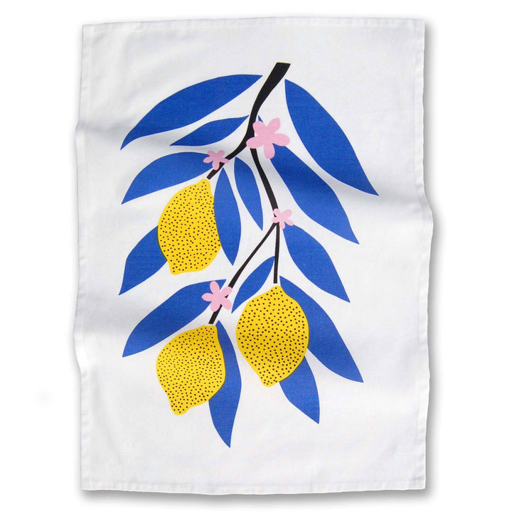 A flat lay of a white cotton tea towel with bright yellow lemons, blue leaves and pale pink flowers