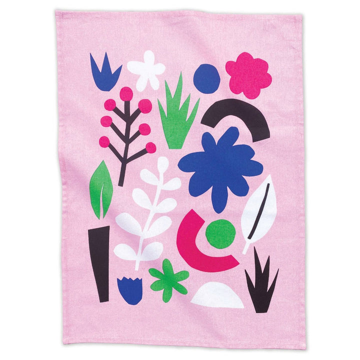 A flat lay of a pale pink cotton tea towel with bright blue, green, fuchsia, black and white geometric shapes and abstract flowers.