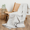 The Birch Bark Reversible Blanket by Mini Tipi, featuring a delicate white birch bark-inspired pattern on a grey background, draped over wooden chair. This reversible blanket is available in Ottawa, Ontario, Canada.