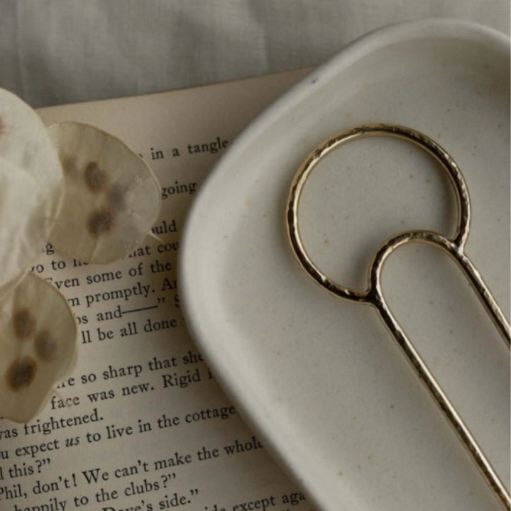 Brass crescent hair fork on ceramic dish with book underneath. 