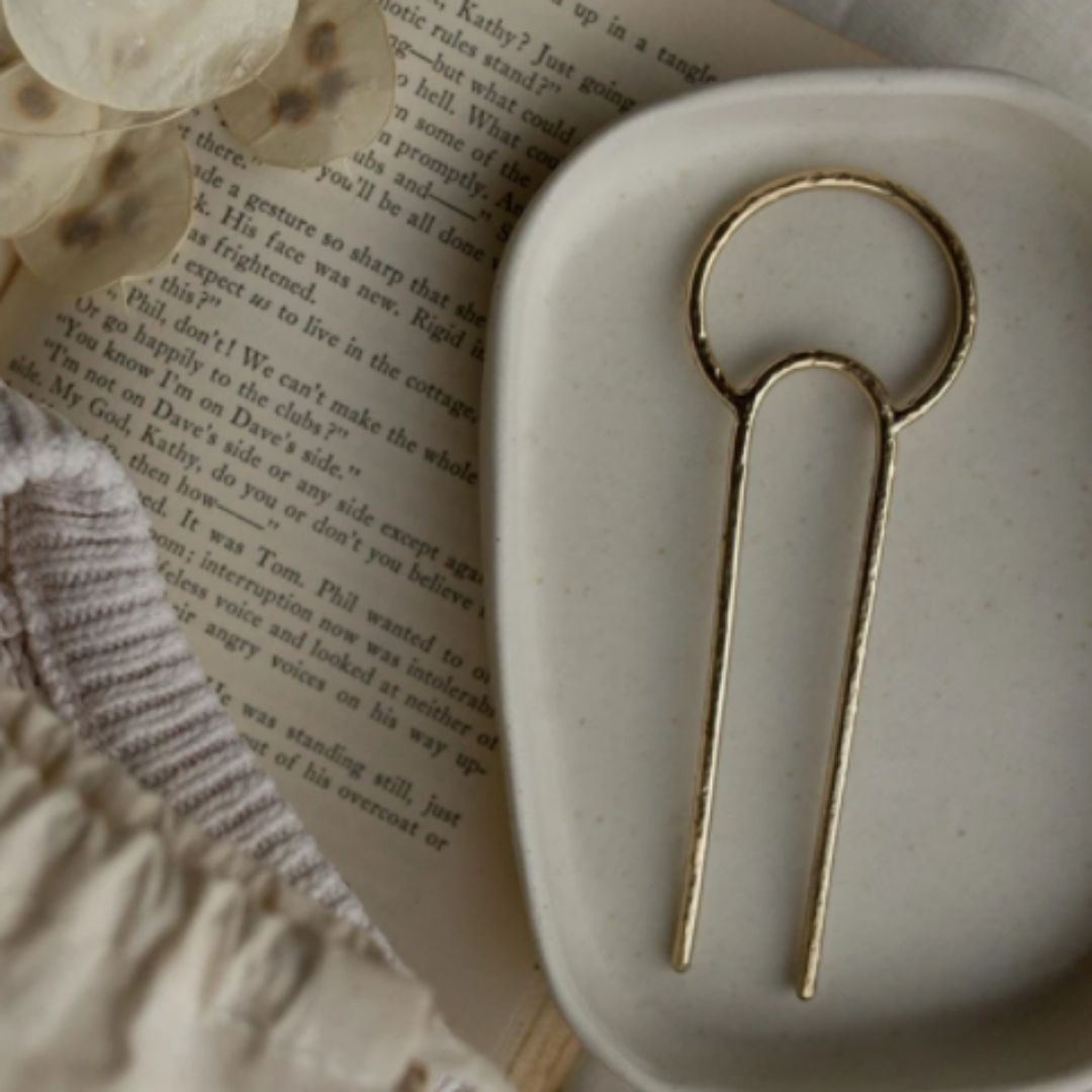 Brass crescent hair fork on ceramic dish with book underneath. 