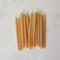 A group of 20 thin, yellow beeswax birthday candles arranged on a white marble surface. The candles have a slightly curved shape and a wick at one end.