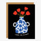 A black card with a white and blue vase with red flowers and the quote 