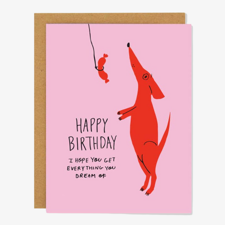 A pink card with red dog standing on hind legs begging for sausage dangling from string, with quote 