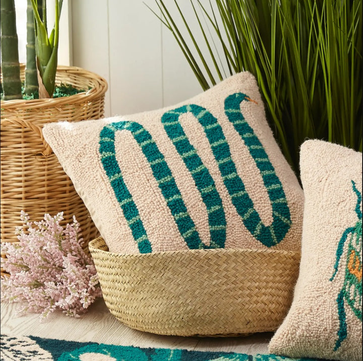 The pillow described in the last picture in a basket next to green plants.