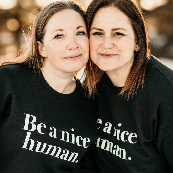 Two woman wearing sweaters that say 