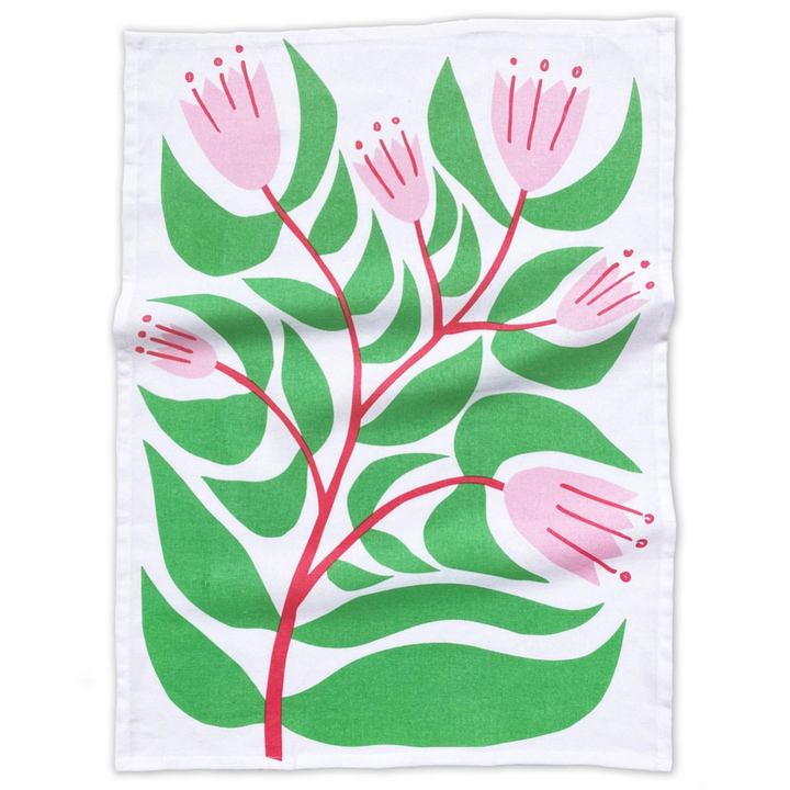 A flat lay image of a white cotton tea towel with an illustration of flowering pink tulips and big green leaves.